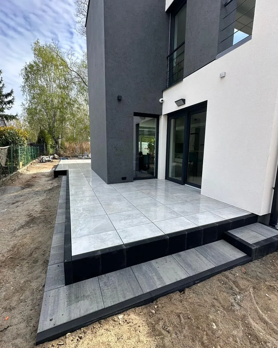 Taras z płyt gresowych 60x60 z cokołem z palisad przy nowoczesnym domu